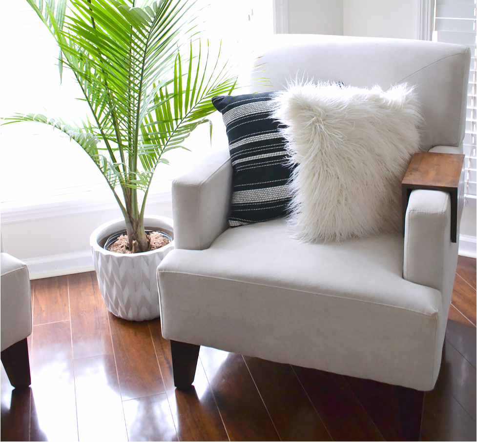 A cream-colored chair in a bright corner with a plant