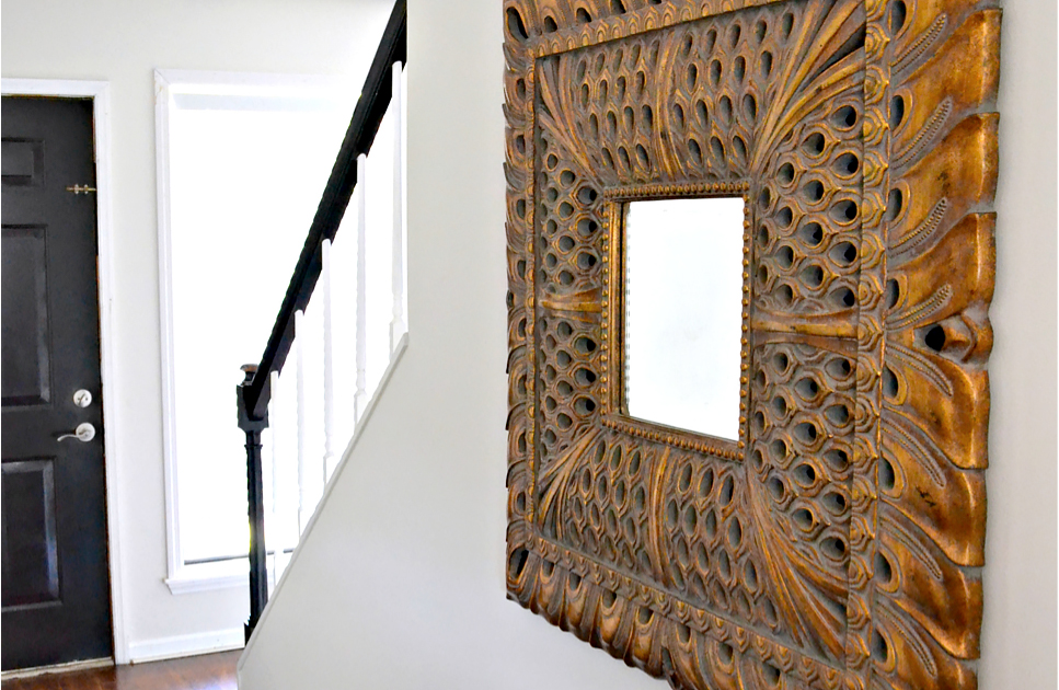 Wood mirror in a white entryway with a black front door