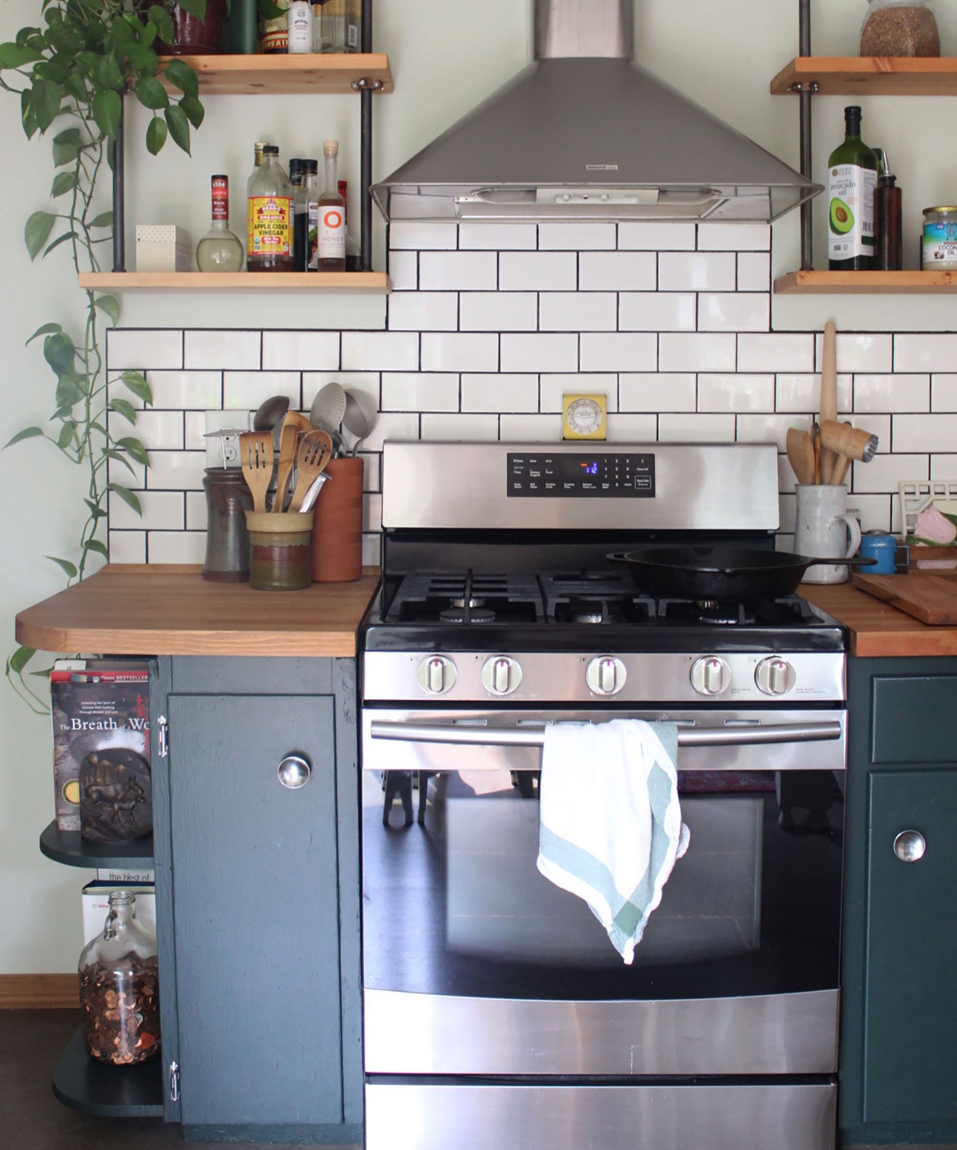Stainless steel stove with hood between dark blue cabinets