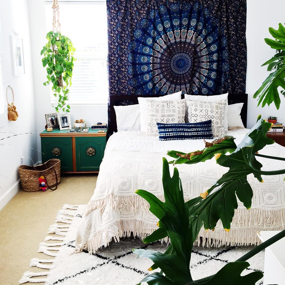A bright bedroom with a blue tapestry and lots of plants