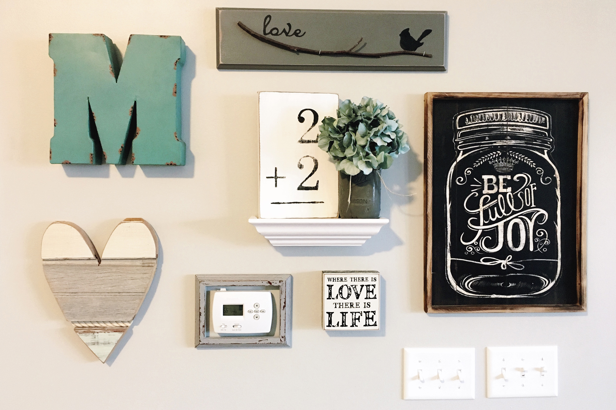 A beige wall with framed thermostat and other paintings
