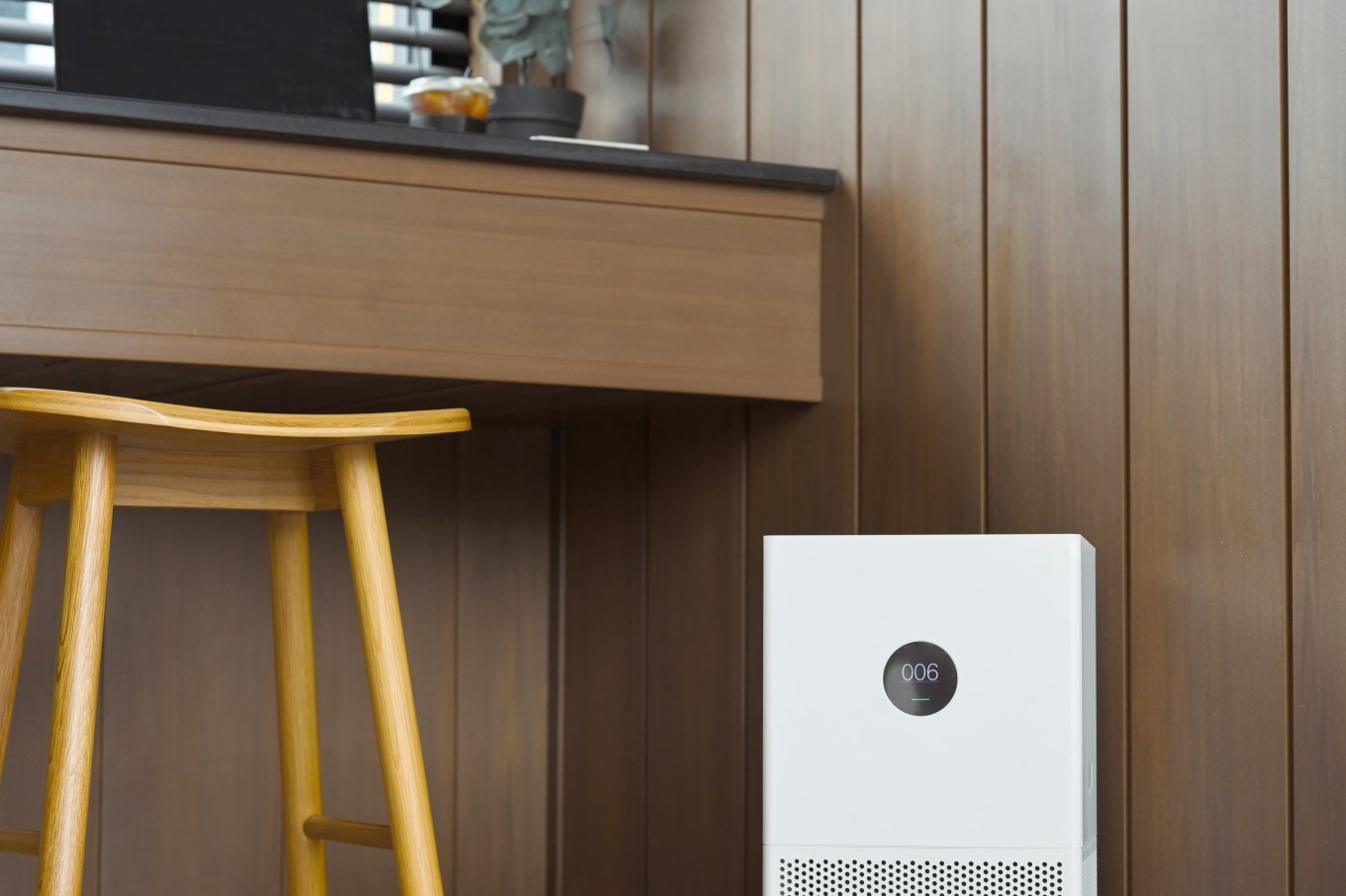 A modern air purifier placed near a wooden desk in a home that's designed with wellness in mind.